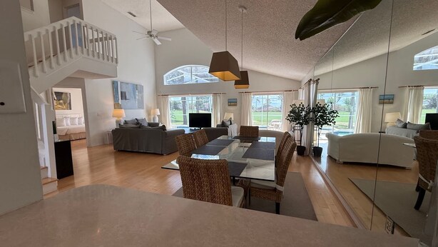 A spacious living area with a high ceiling, a dining table, and a staircase leading to an upper level. - 8th Fairway Pool Villa, Southern Dunes (Haines City)