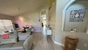 A modern living room with a grey sofa, a wooden cabinet, and a dining area in the background. - Remodeld South Facing Villa - Southern Dunes Golf Course Views (Haines City)