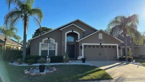 A two-story house with a garage, a front porch, and a small front yard with palm trees and shrubs. - Remodeld South Facing Villa - Southern Dunes Golf Course Views (Haines City)