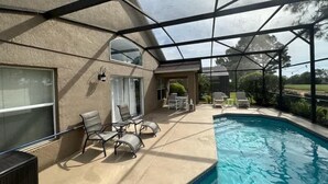 A covered outdoor swimming pool area with lounge chairs and a patio table. - Remodeld South Facing Villa - Southern Dunes Golf Course Views (Haines City)