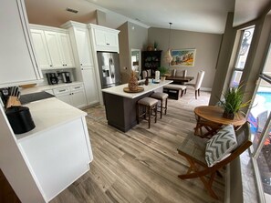 A modern kitchen with white cabinets, a central island, and a dining area with a round table and chairs. - Fully Updated Pool Villa, Southern Dunes (Haines City)