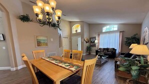 A dining area with a wooden table and chairs, a chandelier, and a living room with a sofa and a lamp. - Private Pool Villa, Many Updates! Southern Dunes (Haines City)