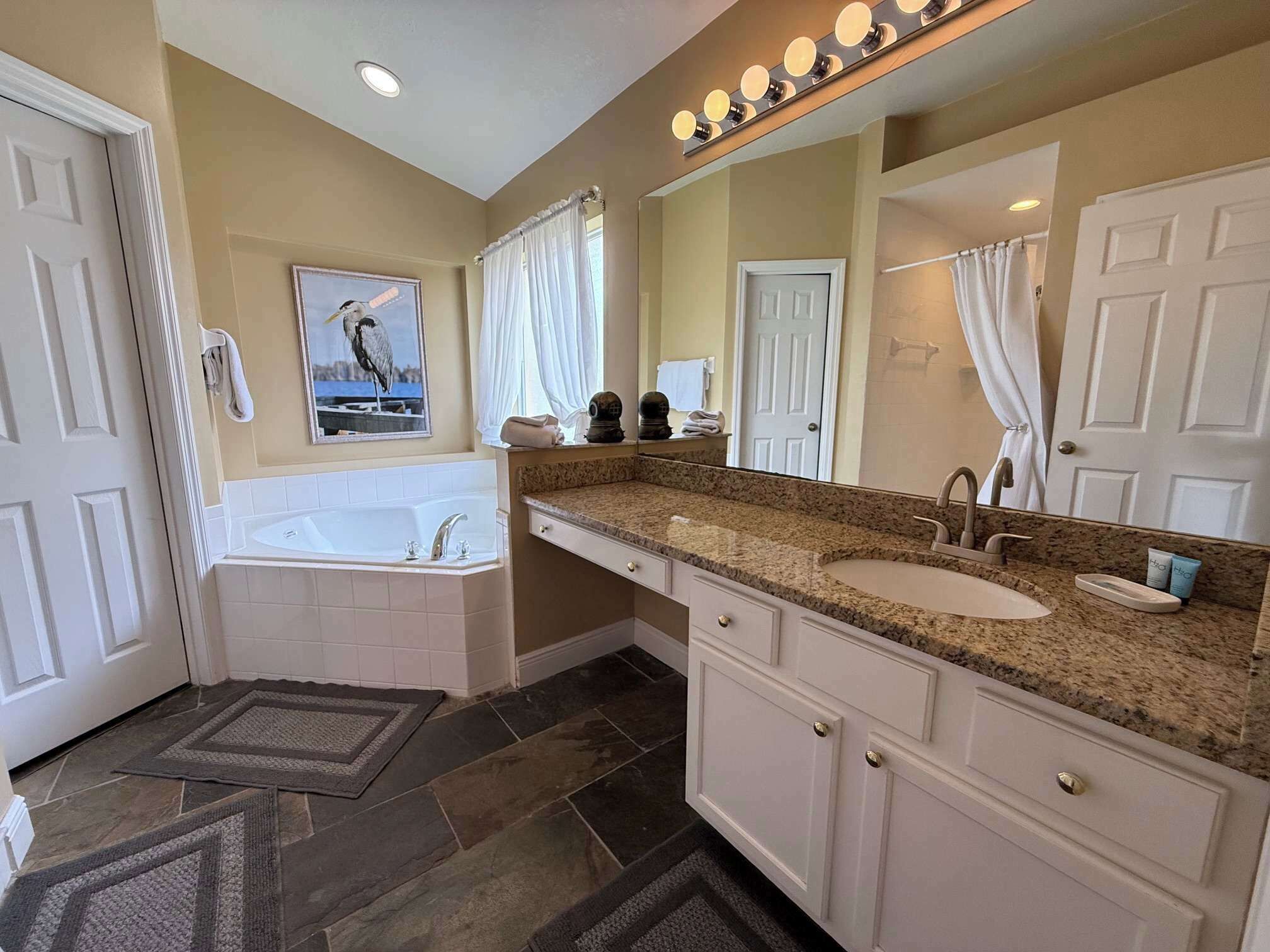 A bathroom with a double sink vanity, a bathtub, a large mirror with lights, and a towel rack.