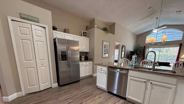 A kitchen with white cabinets, a stainless steel refrigerator, a dishwasher, and a window with a view. - Private Pool Villa, Many Updates! Southern Dunes (Haines City)