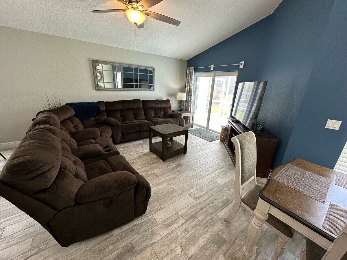 A living room with a sectional sofa, a small table, and a dining table.