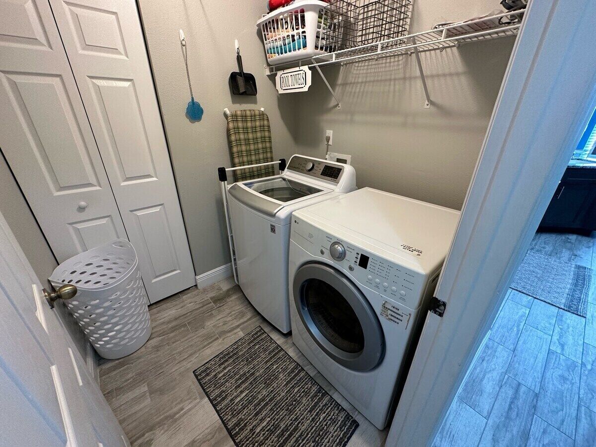 A laundry room with a front-loading washer and dryer, a drying rack, and a basket of laundry.