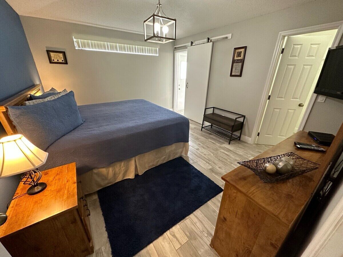 Une chambre à coucher comprenant un lit, une table de chevet, une lampe et un petit bureau avec une télévision et des télécommandes.