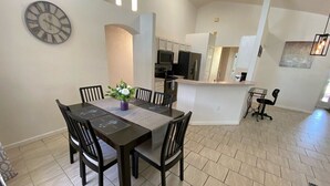 Un coin repas avec une table rectangulaire, six chaises et une horloge au mur.