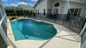 Une piscine à bord incurvé, entourée d’un patio couvert aménagé avec des chaises et des tables.