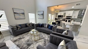 A spacious living area with a grey sofa set, a marble-patterned rug, and a kitchen in the background. - Beautifully Remodeled Home - Southen Dunes Golf Course Views (Haines City)