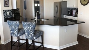 A kitchen with a black countertop, two patterned chairs, a refrigerator, and a clock on the wall. - Private, Large Pool Villa, Southern Dunes, Golf Views, Large Pool Deck (Haines City)