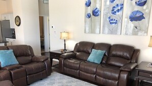 A living room with a brown leather sofa set, a patterned rug, and a wall with abstract blue floral paintings. - Private, Large Pool Villa, Southern Dunes, Golf Views, Large Pool Deck (Haines City)