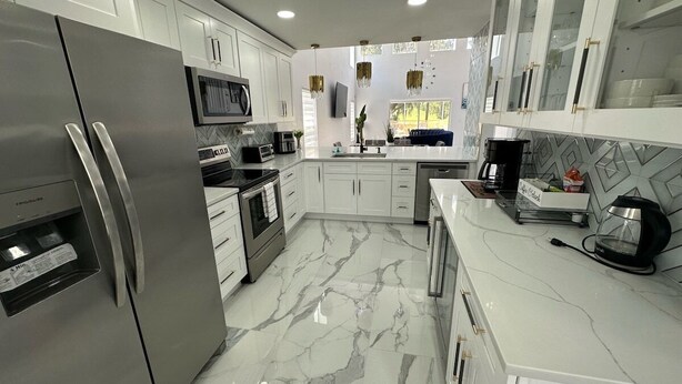 A modern kitchen with stainless steel appliances, white cabinetry, and a marble floor. - Modern, Fully Updated Southern Dunes Home - Golf Course Views (Haines City)