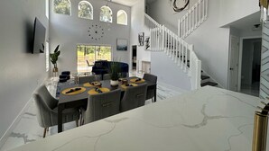 A modern kitchen with a marble countertop, a dining area with a round table, and a staircase with white railings. - Modern, Fully Updated Southern Dunes Home - Golf Course Views (Haines City)