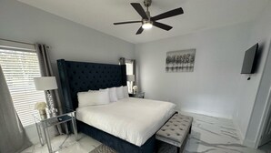 A modern bedroom with a bed, bedside tables, a bench, a ceiling fan, and a painting on the wall. - Modern, Fully Updated Southern Dunes Home - Golf Course Views (Haines City)