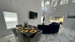 A modern dining area with a marble floor, a dark dining table with yellow placemats, and grey upholstered chairs. - Modern, Fully Updated Southern Dunes Home - Golf Course Views (Haines City)