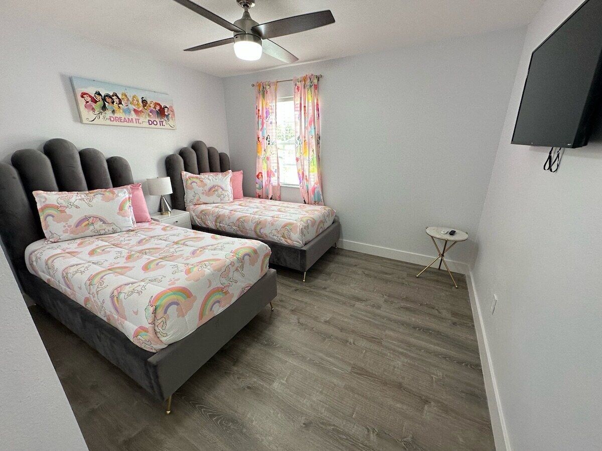 A bedroom with two beds, a ceiling fan, a small table, and a TV mounted on the wall.