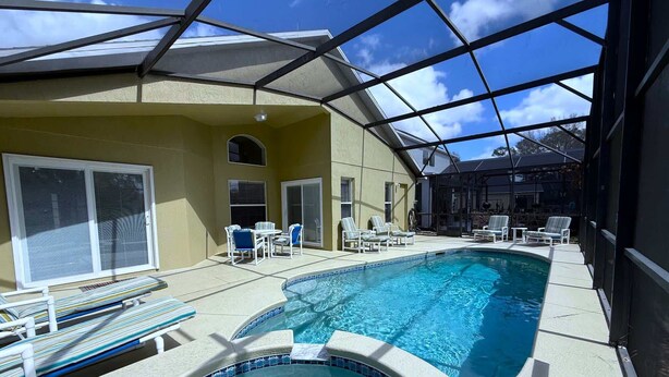 A pool area with a glass-enclosed structure, lounge chairs, and a table. - South Facing Golf Course Views, Southern Dunes Villa (Haines City)