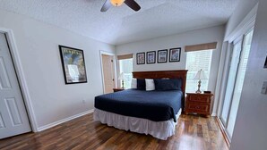 A bedroom with a large bed, wooden flooring, a ceiling fan, and a window with blinds. - South Facing Golf Course Views, Southern Dunes Villa (Haines City)