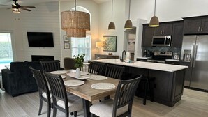 A modern kitchen with dark cabinetry, a central island, and a dining area with a wooden table and chairs.