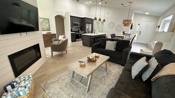 A modern living room with a flat-screen TV, a fireplace, a dining area with a kitchen in the background, and a cozy seating area with a sofa and a coffee table.