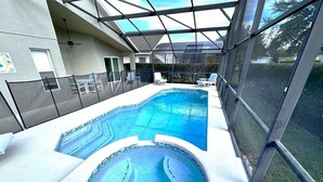 An indoor swimming pool with a hot tub, surrounded by glass walls and a covered area with chairs.