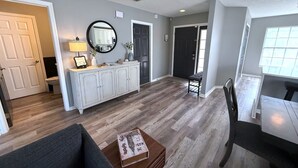A spacious living area with hardwood flooring, a white cabinet, a round mirror, and a dining table with chairs. - Updated Southern Dunes Pool Home (Haines City)