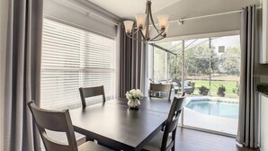 Comedor con mesa, sillas, una araña y vista a una piscina.