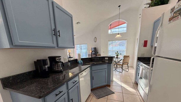 Cocina moderna con armarios azul claro, encimera negra y lavavajillas integrado. Cuenta con un comedor con mesa y sillas, y una ventana que proporciona luz natural.