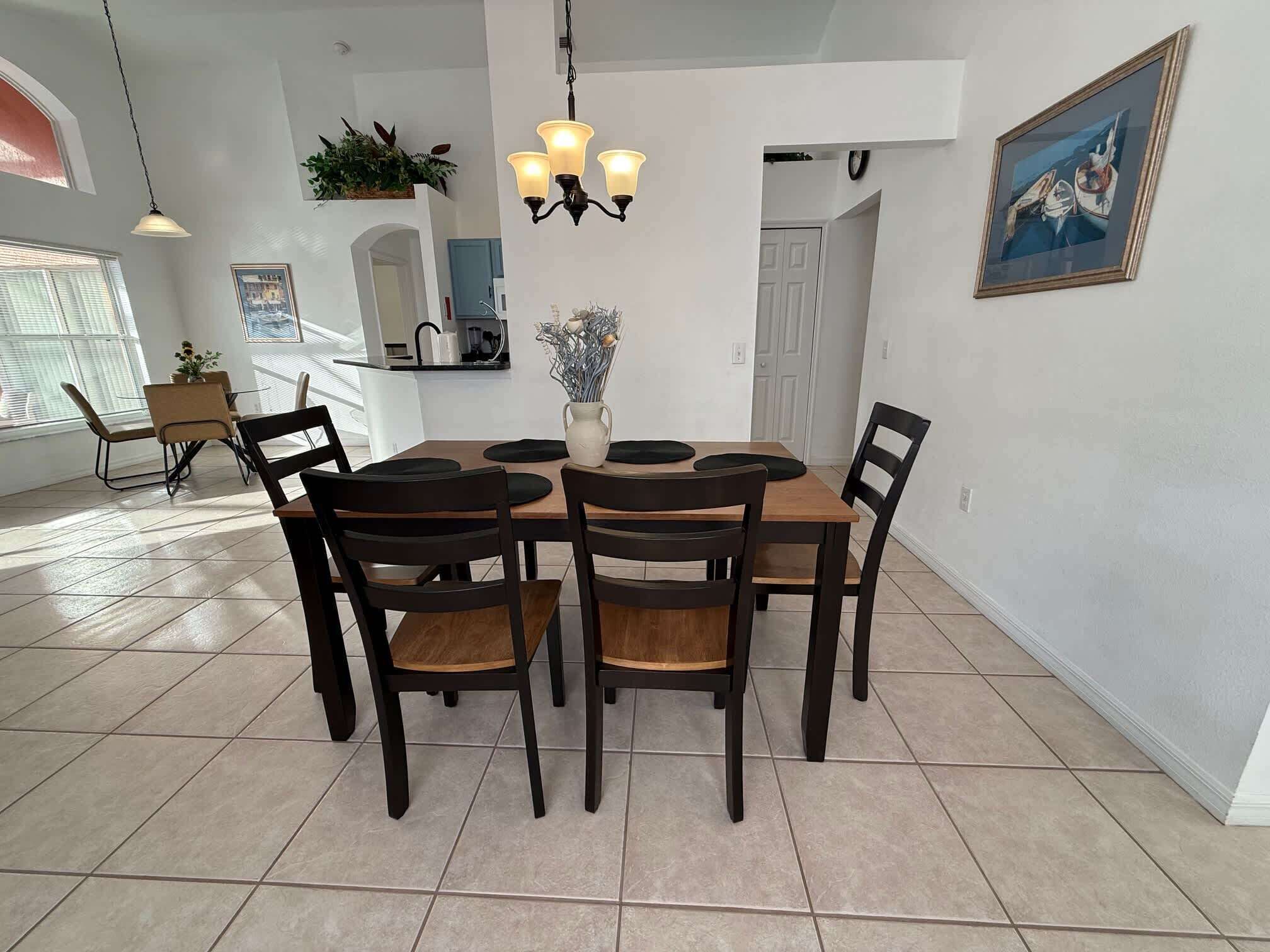 A dining area with a wooden table and chairs, a chandelier, and a painting on the wall.