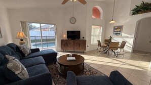Una sala de estar con un sofá, una mesa de centro, un televisor sobre un mueble bajo y un comedor con sillas y una mesa.