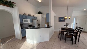 Una cocina amplia con gabinetes azules, una isla blanca y una zona de comedor con mesa y sillas.