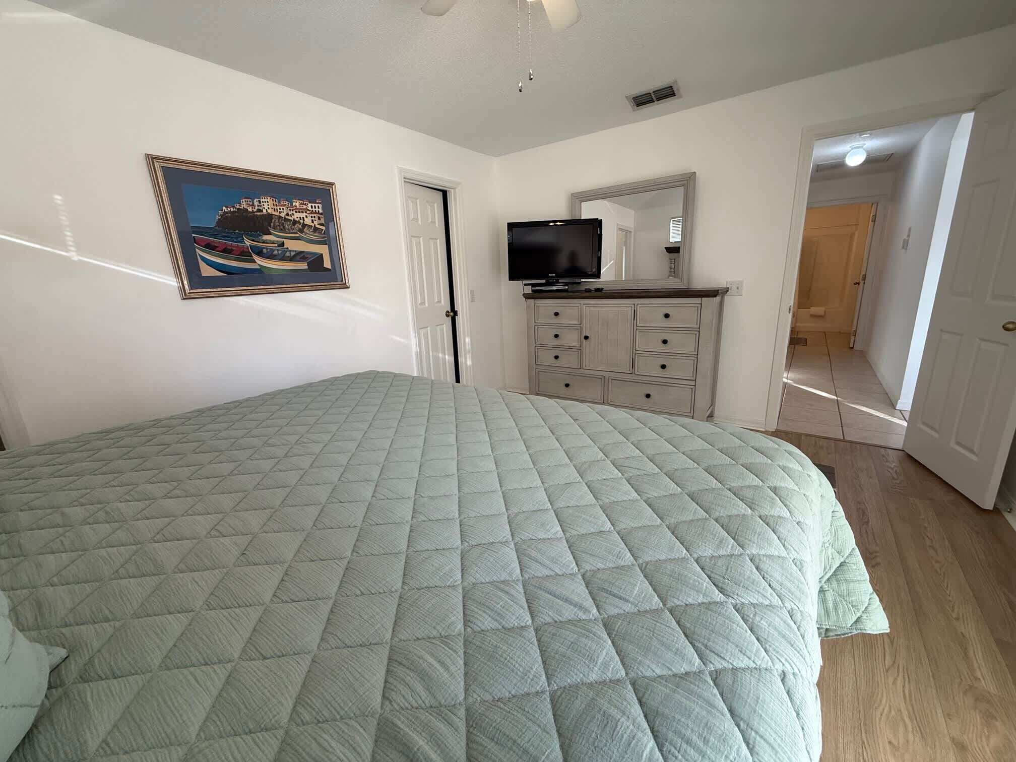 Une chambre à coucher avec un lit, une commode, un téléviseur et un tableau encadré au mur.