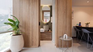 Ein modernes Hotelzimmer mit einer großen Kübelpflanze, einem kleinen runden Tisch und einer Sitzecke mit Sesseln.