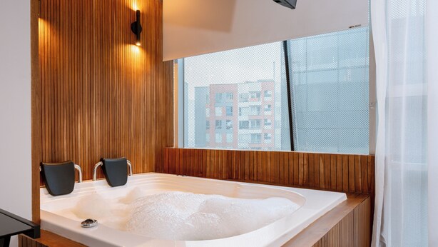 Ein modernes Badezimmer mit einer Holzpaneelwand, einer großzügigen Badewanne und einem Fenster mit Blick auf die Stadt.