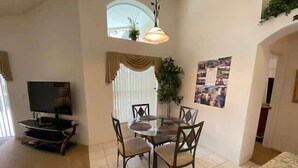 Zona pranzo con tavolo rotondo e sedie, televisore su un mobile e finestra con tende.