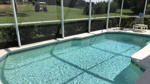 Una piscina cristallina con bordo piastrellato, circondata da un muro bianco e una struttura in vetro.