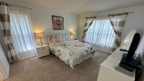Ein Schlafzimmer mit einem Bett, Nachttischen, einem Schreibtisch mit Computer und Vorhängen.