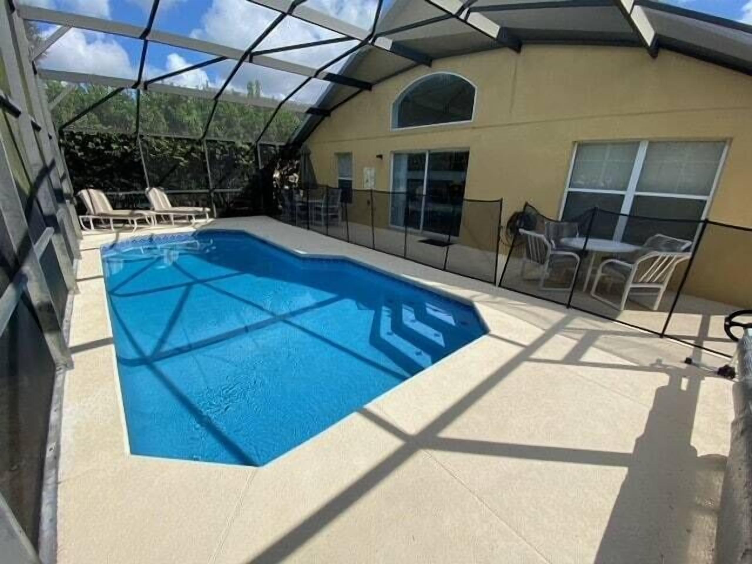 A covered outdoor swimming pool with a geometric glass roof, surrounded by lounge chairs and a patio area.
