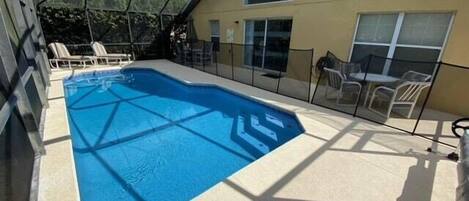 A covered outdoor swimming pool with a geometric glass roof, surrounded by lounge chairs and a patio area.