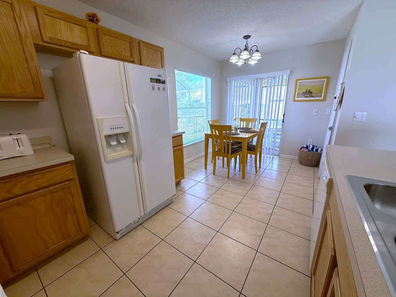 A kitchen with wooden cabinets, a white refrigerator, a dining table with chairs, and a window with blinds.