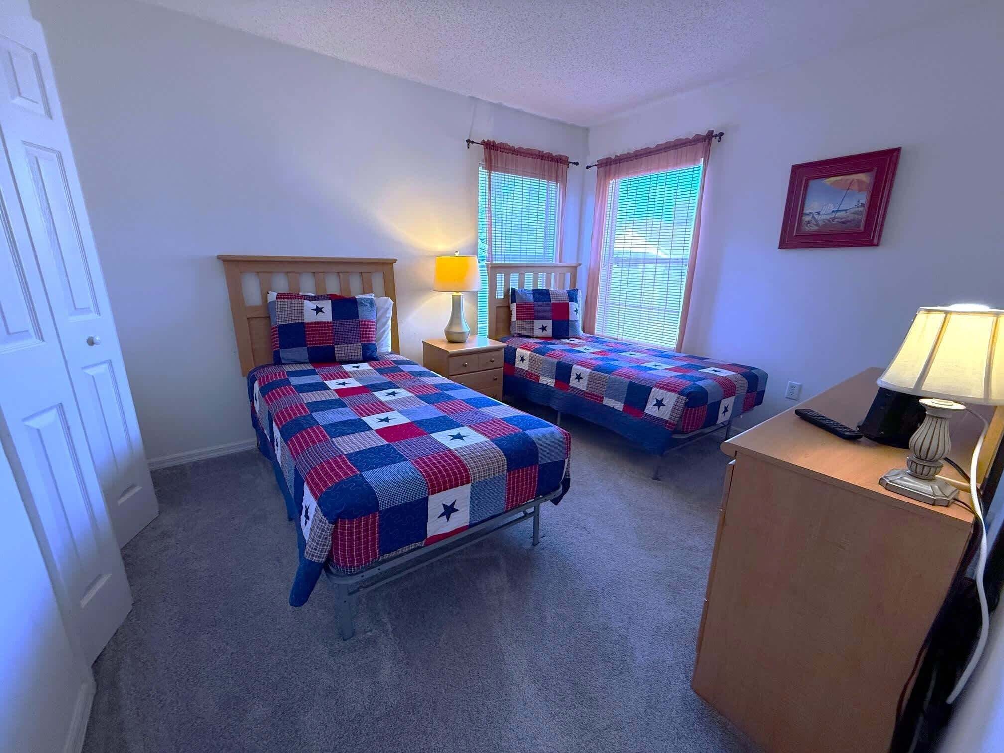 A bedroom with two beds, a nightstand, a desk, and a lamp.