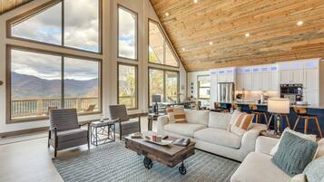 Un vaste espace de vie avec une grande fenêtre donnant sur les montagnes, un coin salon confortable et une cuisine moderne en arrière-plan.