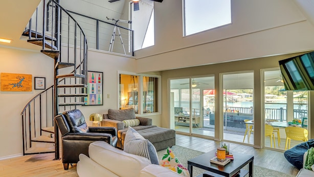 A spacious living area with a spiral staircase, a balcony with outdoor seating, and large windows providing views of the outside. - Lakefront Home w/ Private Dock in Graford! (Graford)