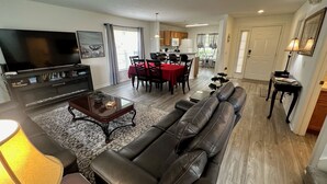 A living room with a sofa, TV, and dining area with a red tablecloth. - Beautiful 3 Bedroom Pool Villa in Southern Dunes (Haines City)