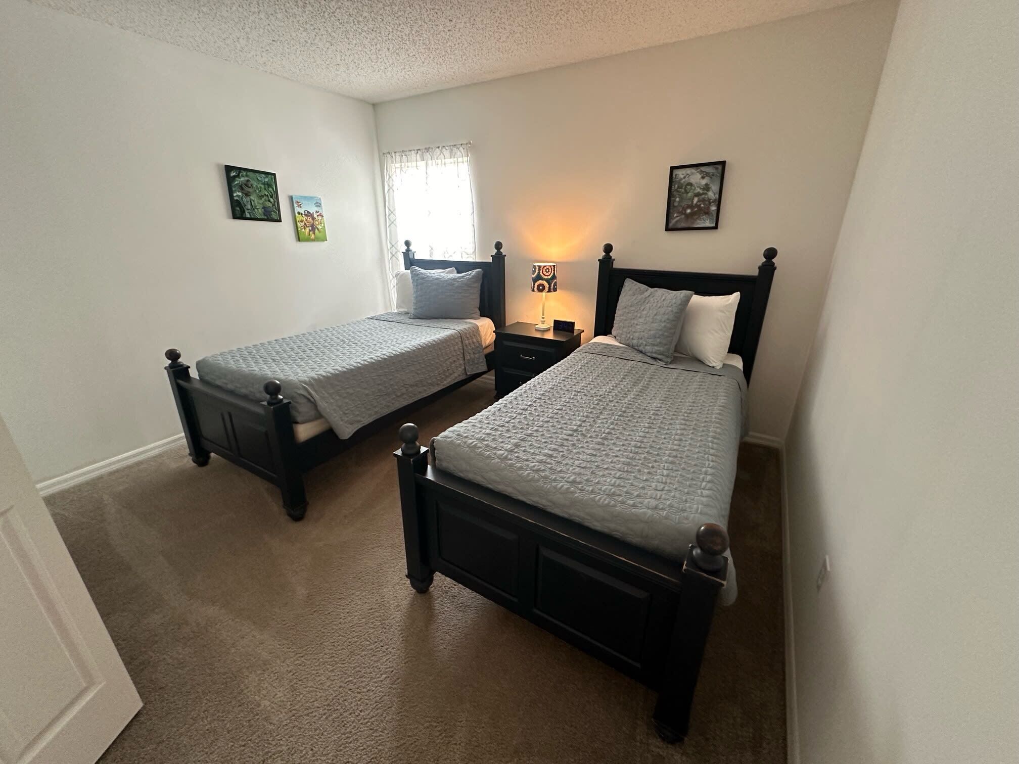 A bedroom with two single beds, a nightstand with a lamp, and a window with curtains.