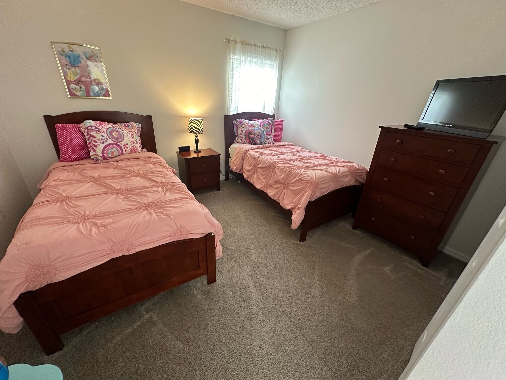 A bedroom with two beds, a dresser, a TV, and a lamp.
