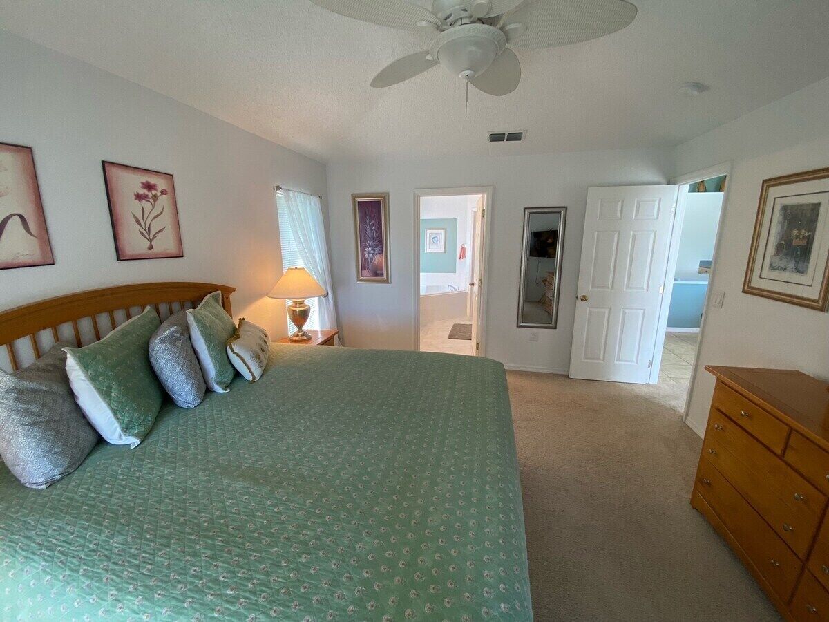 A bedroom with a bed, a dresser, a ceiling fan, and a door leading to another room.