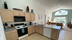 A kitchen with beige cabinets, a black stove, and a dishwasher. There is a window with curtains and a view of greenery outside. - Golf Course Views, South Facing Pool Villa (Haines City)