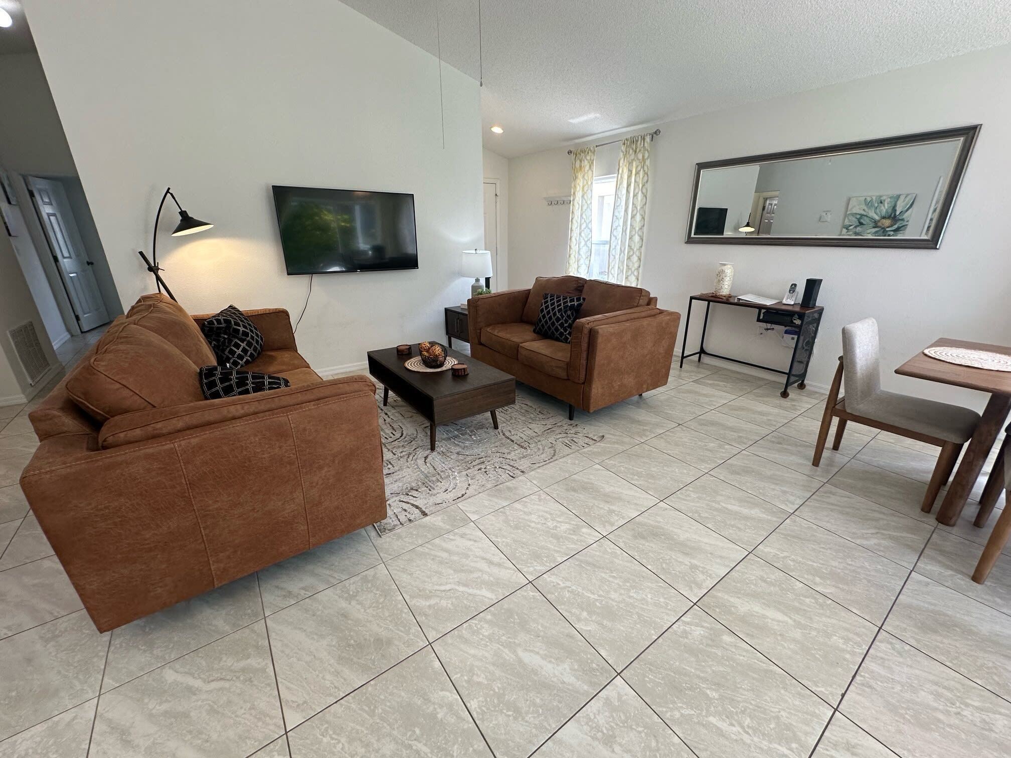 A living room with two brown sofas, a coffee table, a TV, a desk with a chair, and a large mirror.